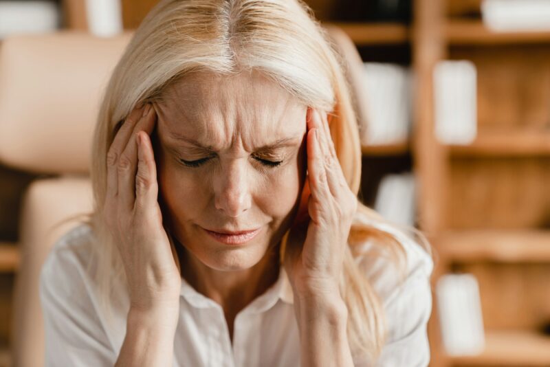 A woman with a pained expression, rubbing her temples to cope with the discomfort of a migraine.
